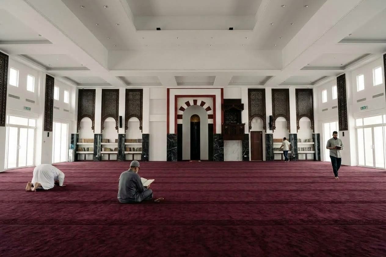 The prayer hall of Masjid Baru RPN Kg Rimba, with the mihrab in a red and white banded arch and a carved timber mimbar